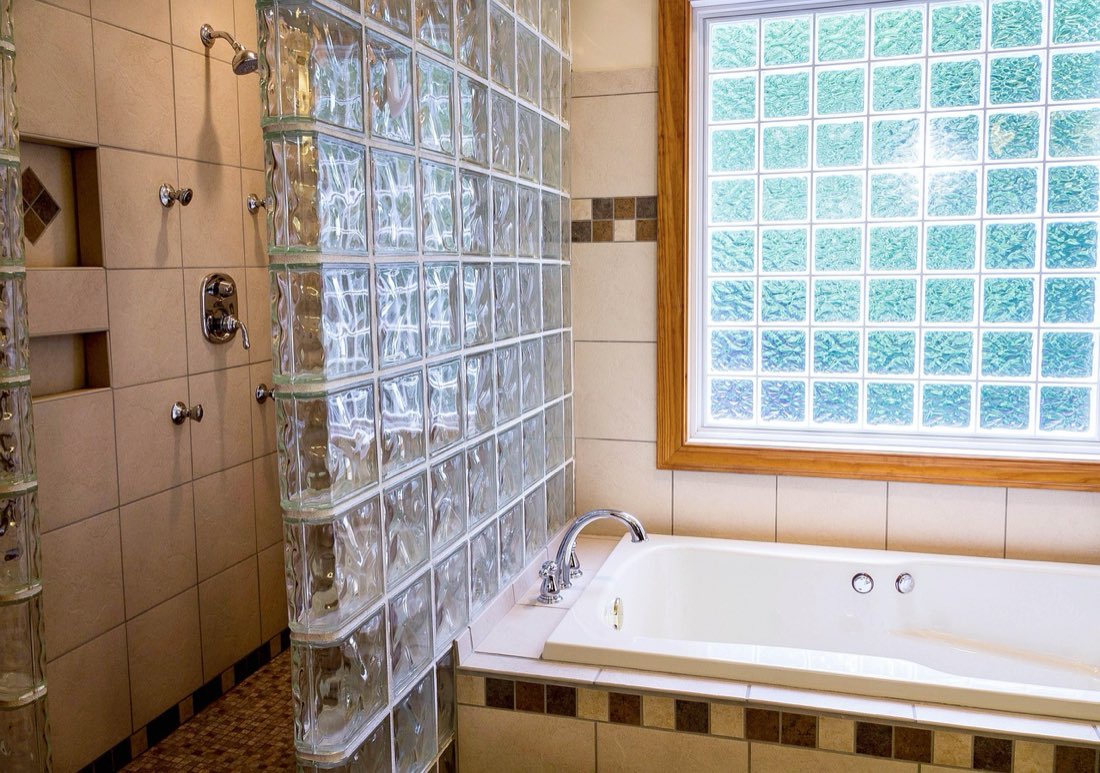 A bathroom with warm ceramic tile, a glass-block accent wall and a deep soaking tub