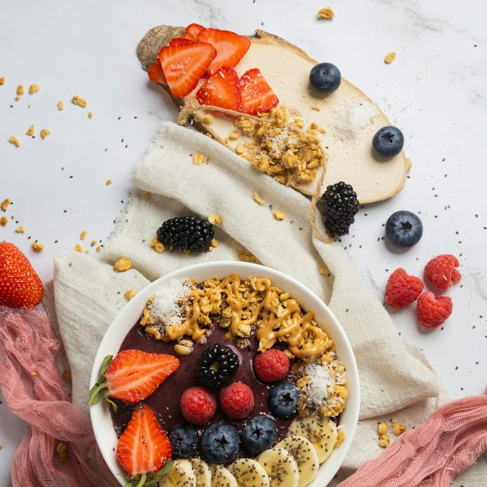 An açaí bowl topped with granola, sliced banana, kiwi, and a drizzle of honey on a light wooden surface