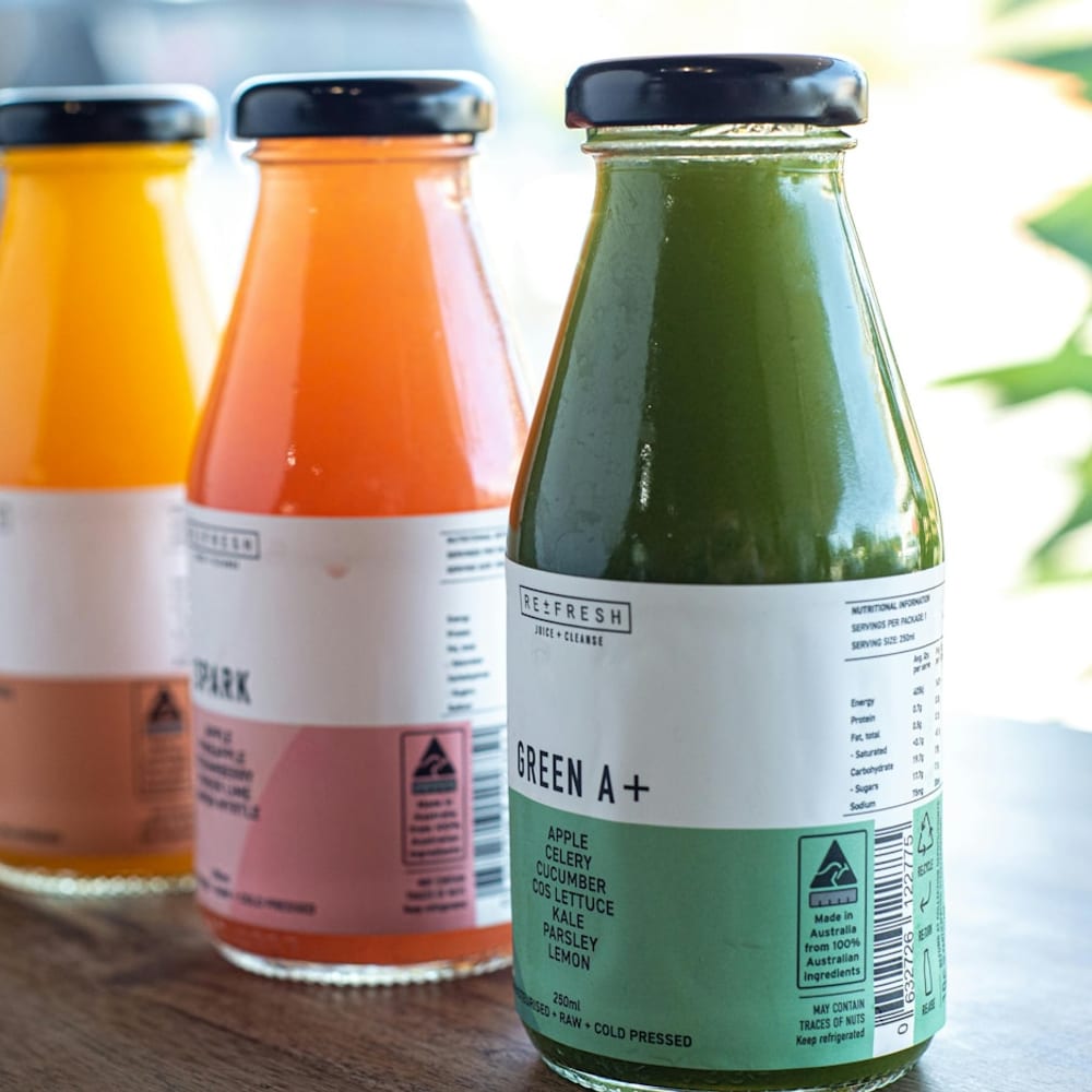 Rows of freshly cold-pressed green juice bottles lined up on a stainless steel counter, morning light streaming in