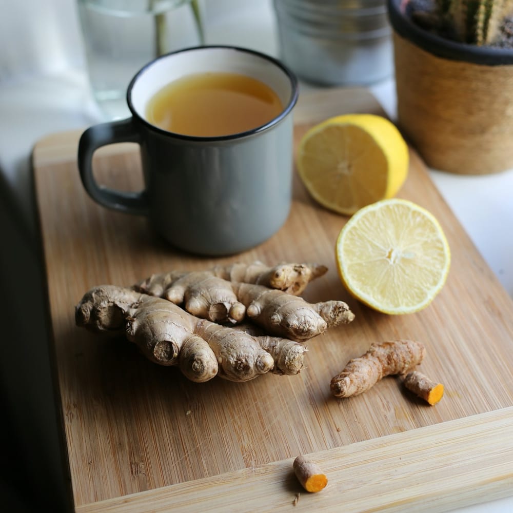 A flat lay of fresh ginger, turmeric root, lemons, and cayenne peppers on a white marble surface
