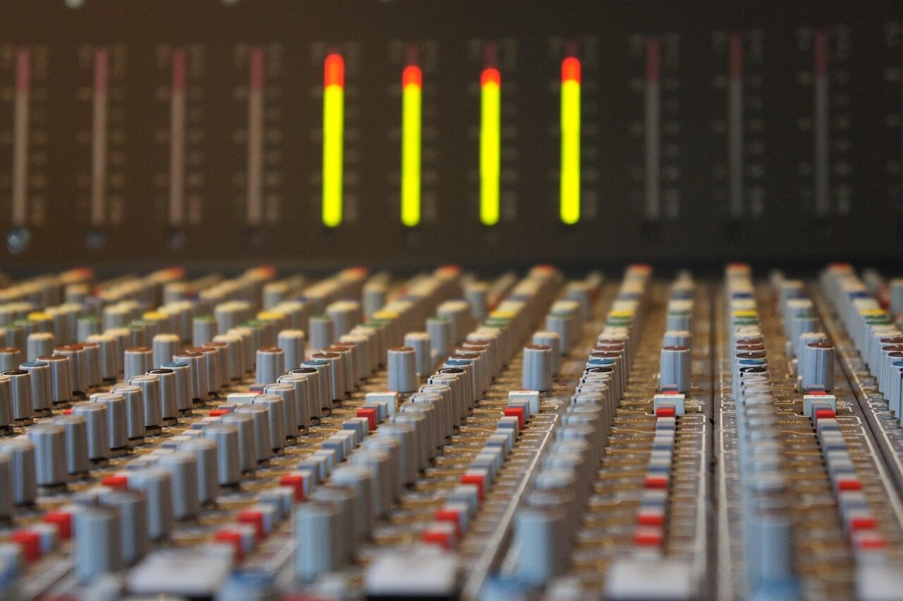 A large analogue mixing console shot along the rows of faders and knobs, with four channel meters lit yellow and red behind them.