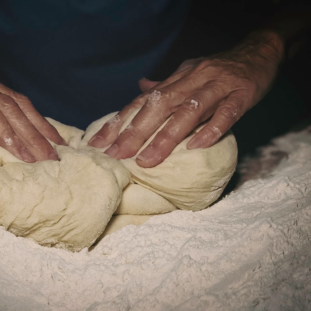 Hands shaping laminated croissant dough on a cold marble surface in morning light