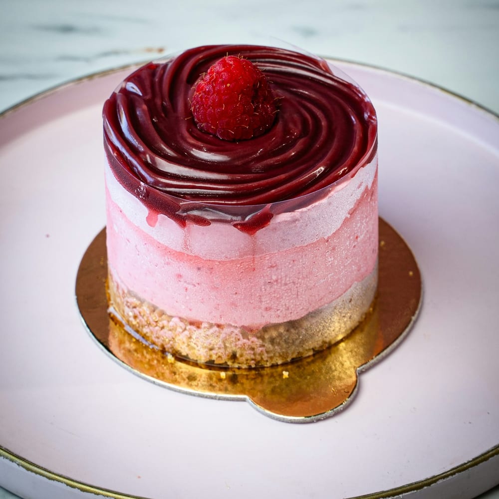 A champagne-rose entremet with blush mirror glaze on a marble plinth, dusted with edible silver