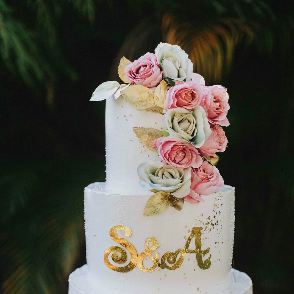A three-tier bespoke wedding gâteau decorated with sugar roses and gold leaf in a patisserie salon