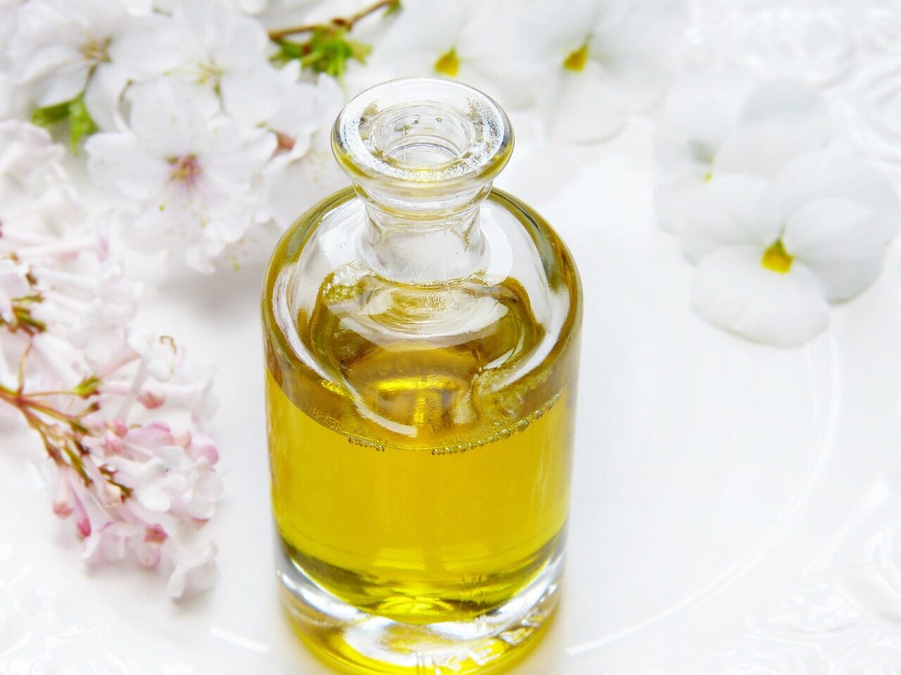 A small glass bottle of golden oil with white blossom behind it