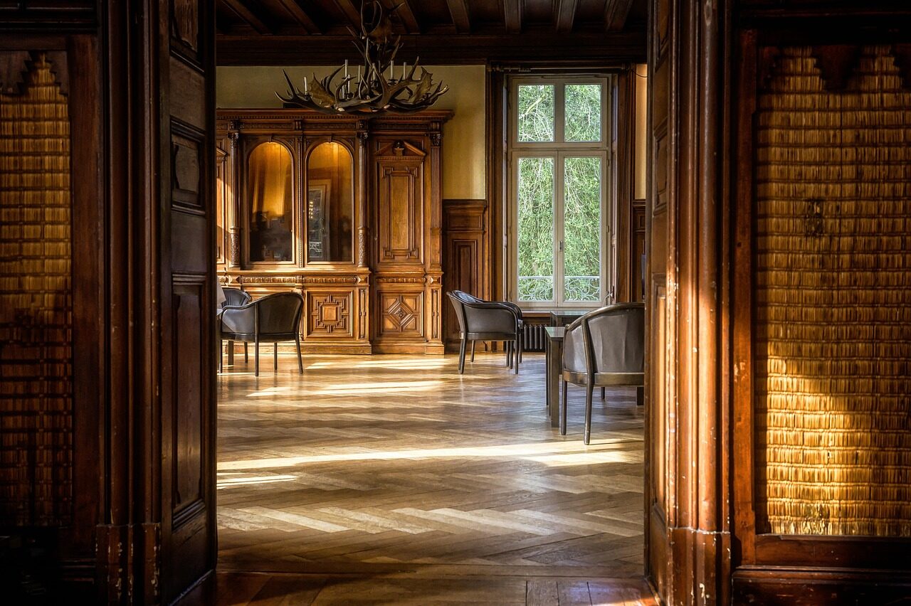 A dark wood-panelled hallway looking through open double doors into a parquet-floored room