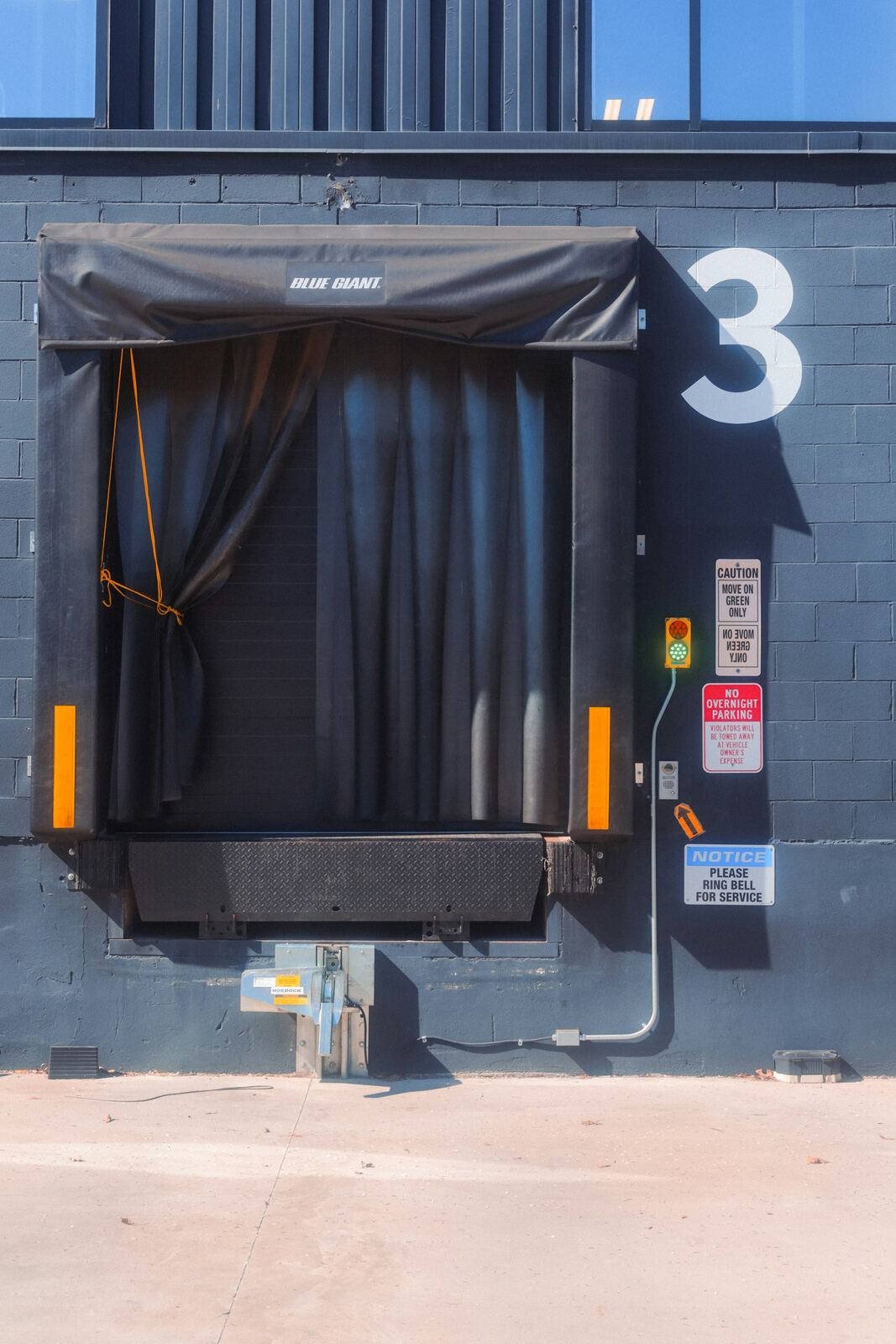A closed loading-dock door with a rubber weather seal, warning signage and a traffic-light indicator beside it