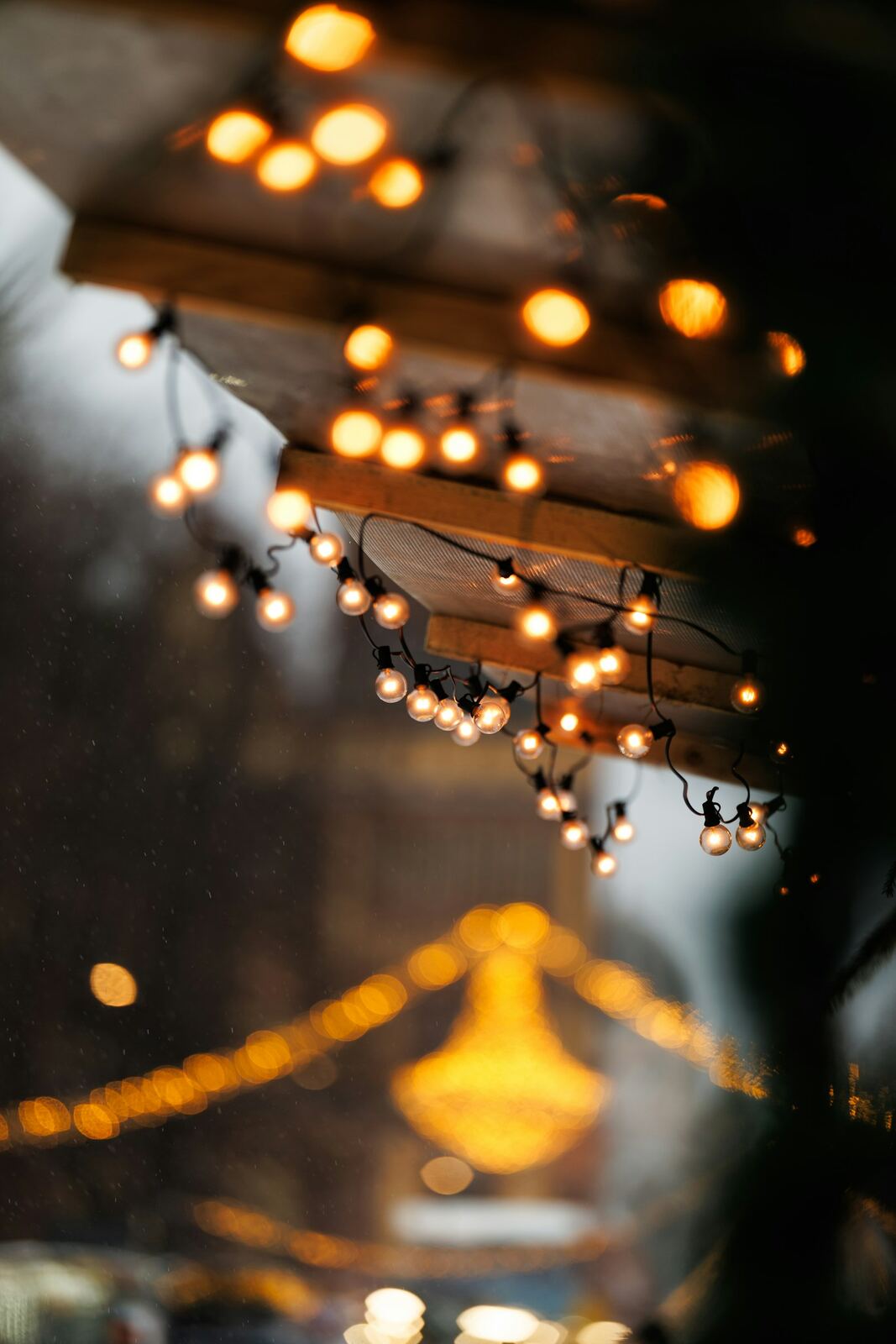 Warm festoon string lights strung along a market stall awning, glowing against a dark evening sky