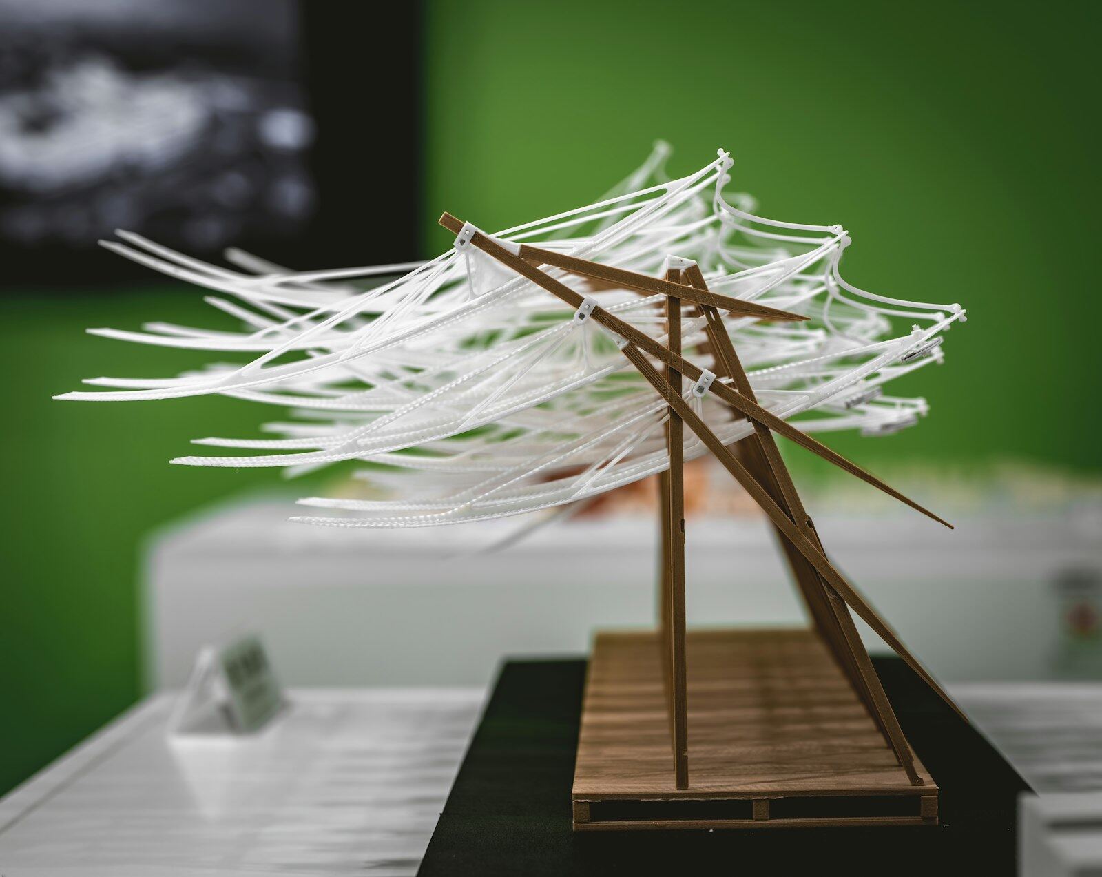 An abstract white architectural model made of curved card strips on a wooden base, shown against a plain background
