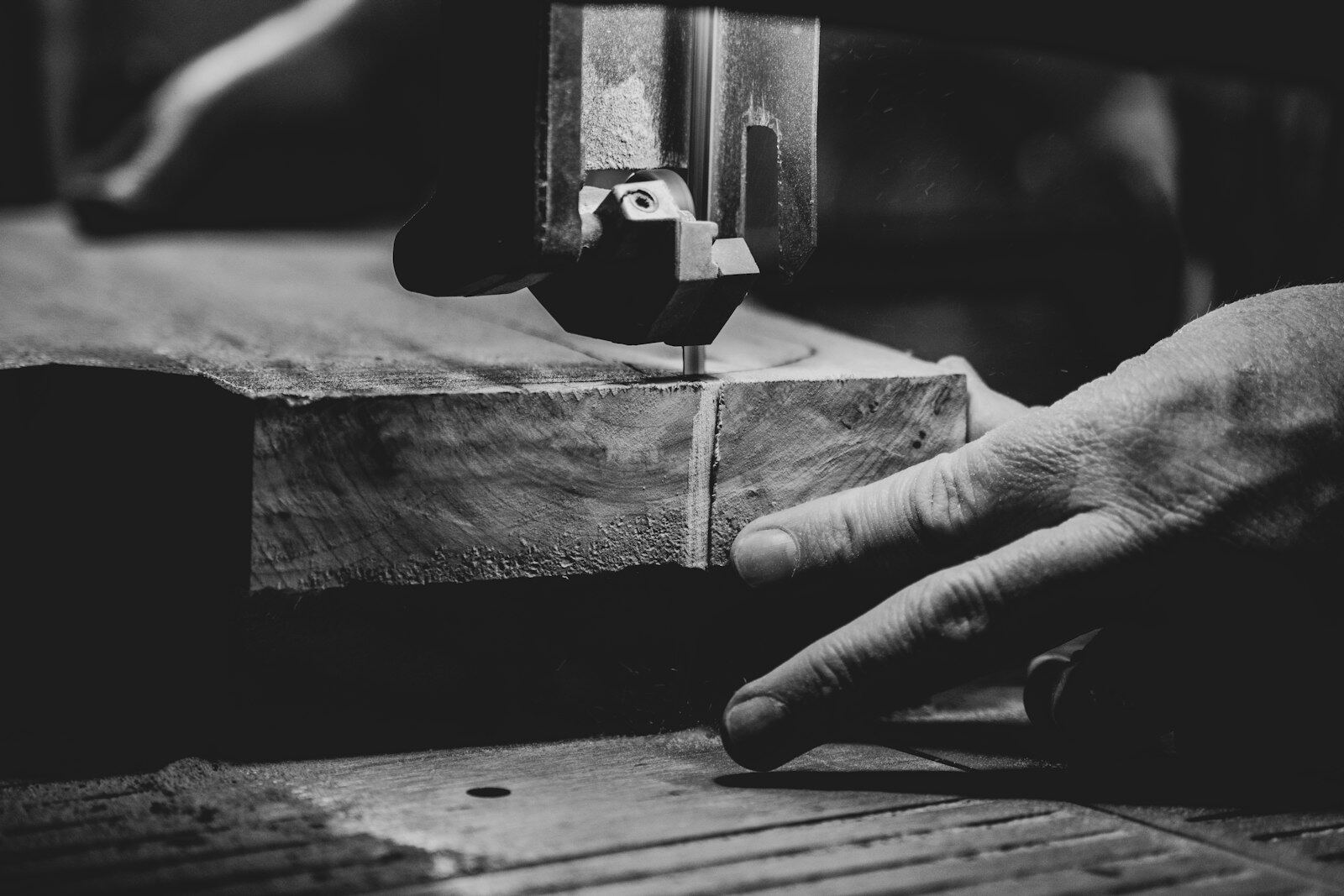 Close-up of a band saw cutting a block of wood, with a hand steadying the timber