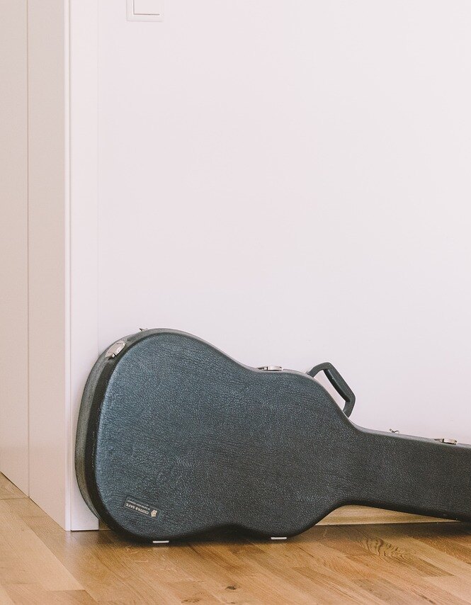 A hard guitar case lying on a wooden floor against a plain white wall.