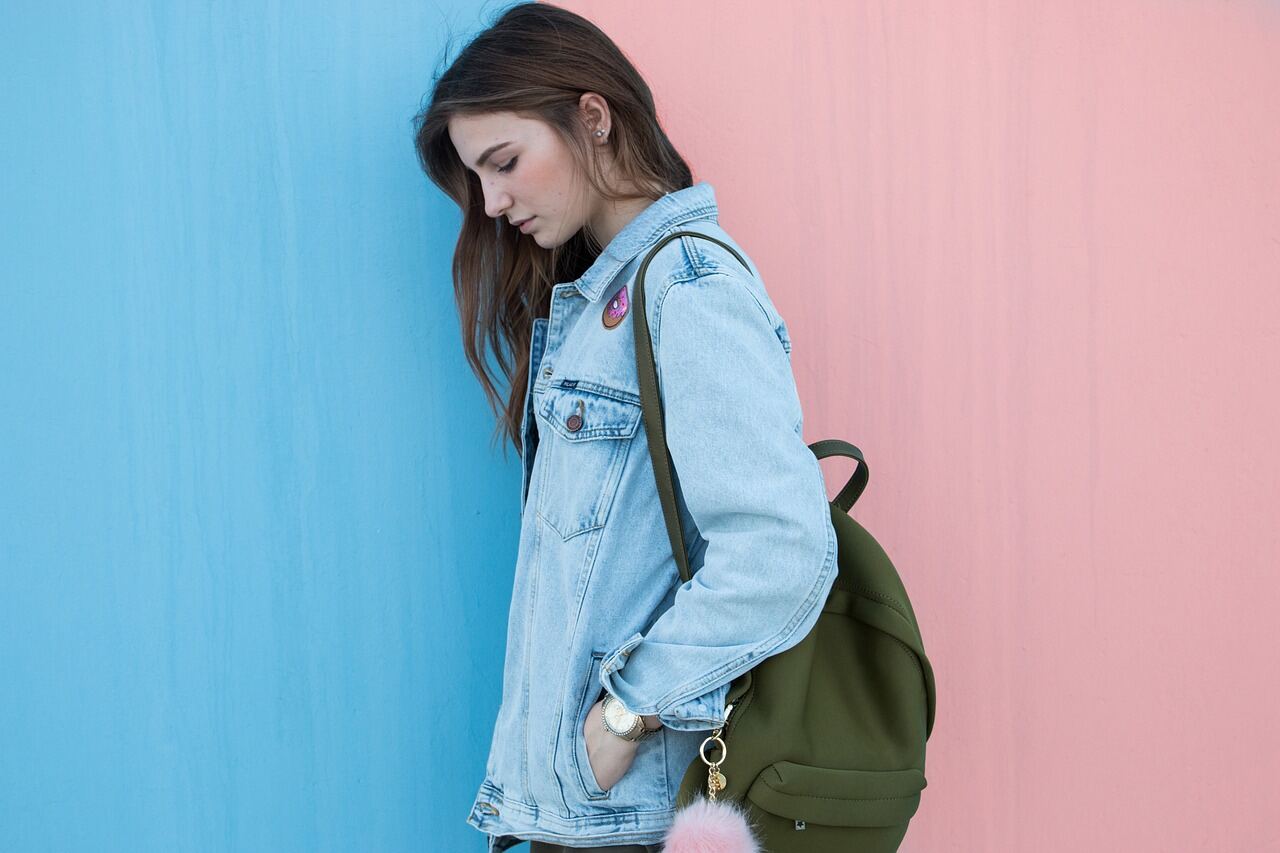 A woman in a denim jacket carrying a canvas backpack, photographed street-style for a campaign
