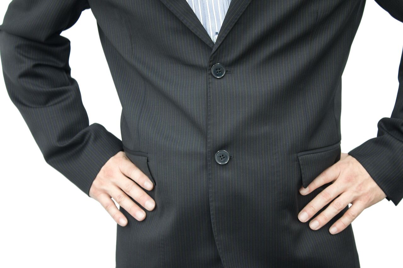 A man in a tailored two-piece suit photographed full-length against a plain studio background
