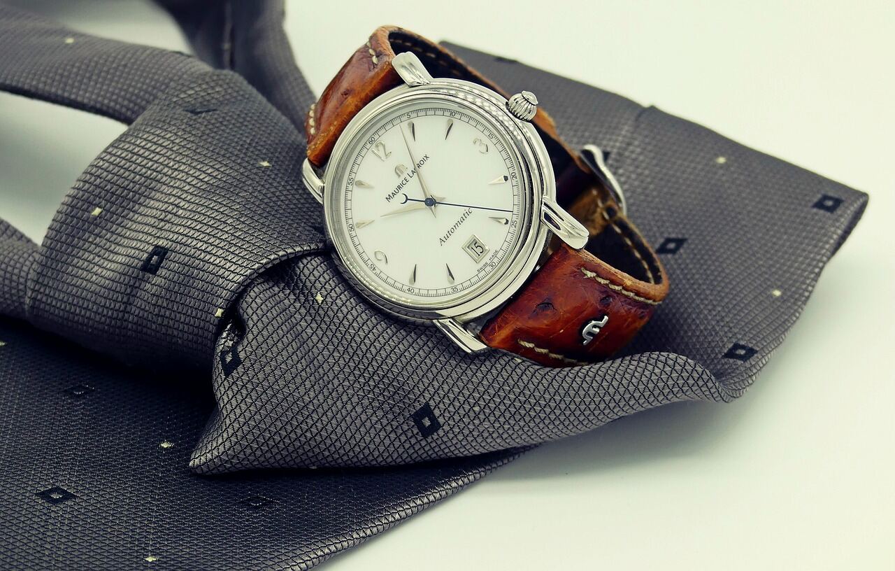 A wristwatch and necktie arranged as a flat lay for a press-day capsule story