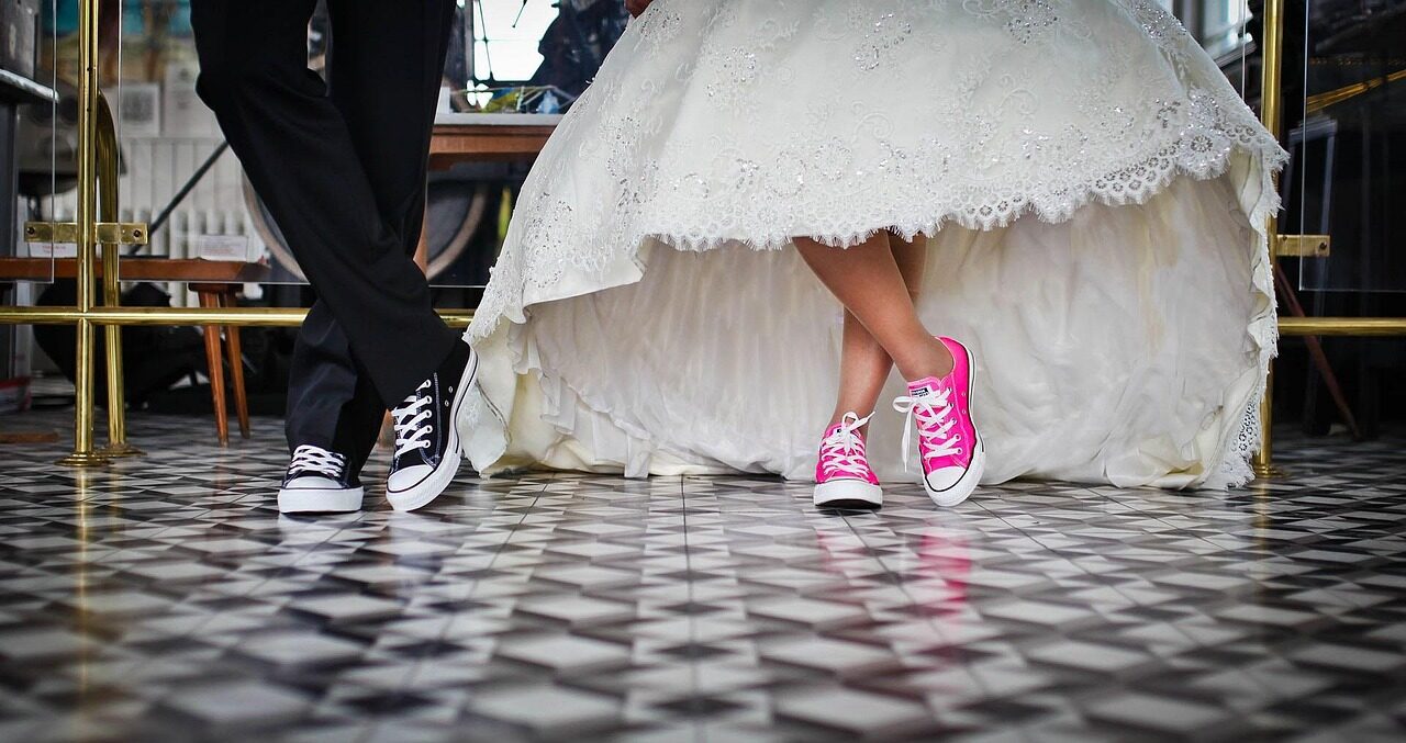Trainers worn under the hem of a wedding dress on a chequerboard floor