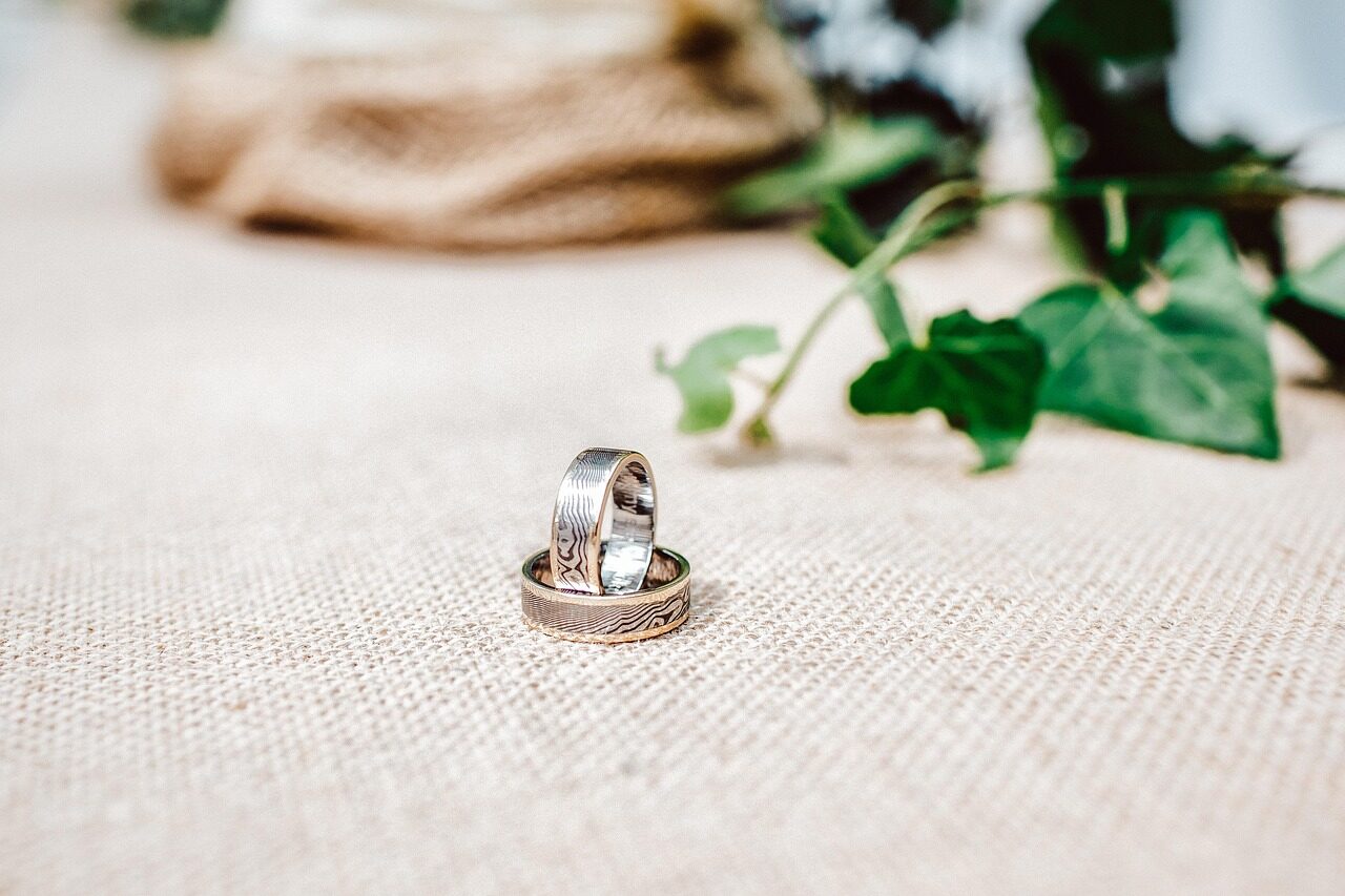 Two wedding rings resting on linen beside a sprig of greenery
