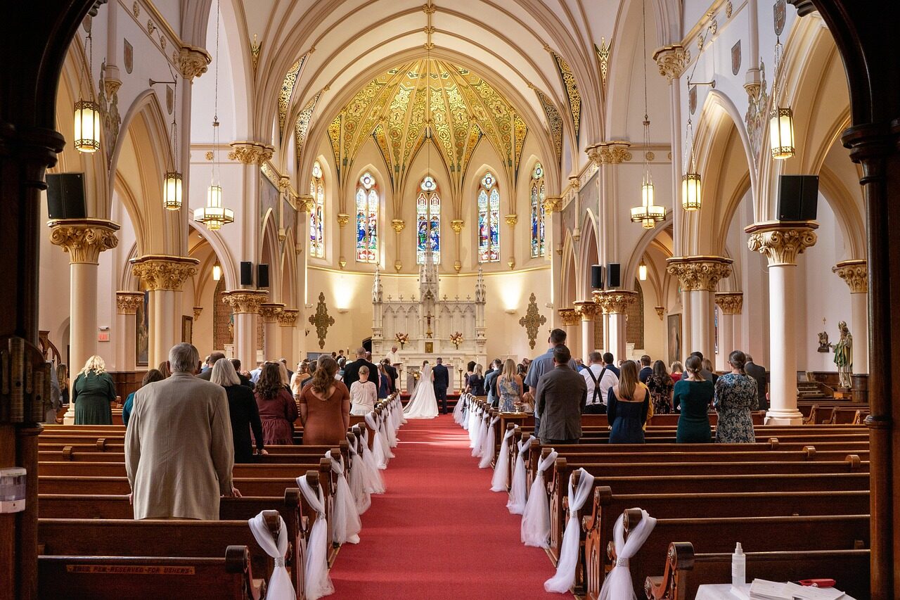 A cathedral interior with a red aisle carpet and guests already seated