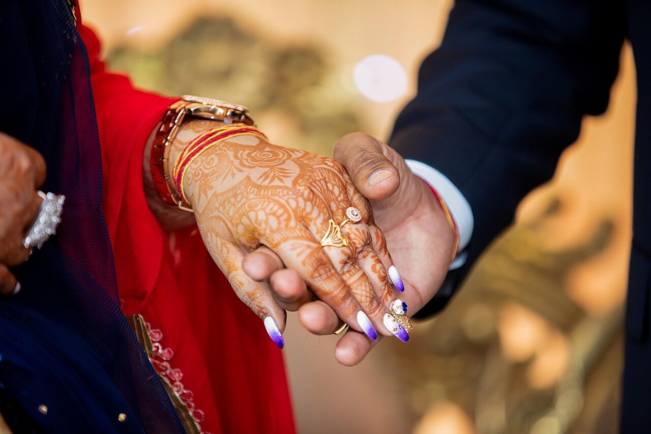Hands decorated with mehndi resting together, one in a red sleeve