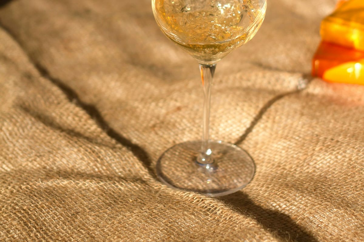 A deep amber glass of orange wine glowing against dark velvet banquette seating, candlelit table in background