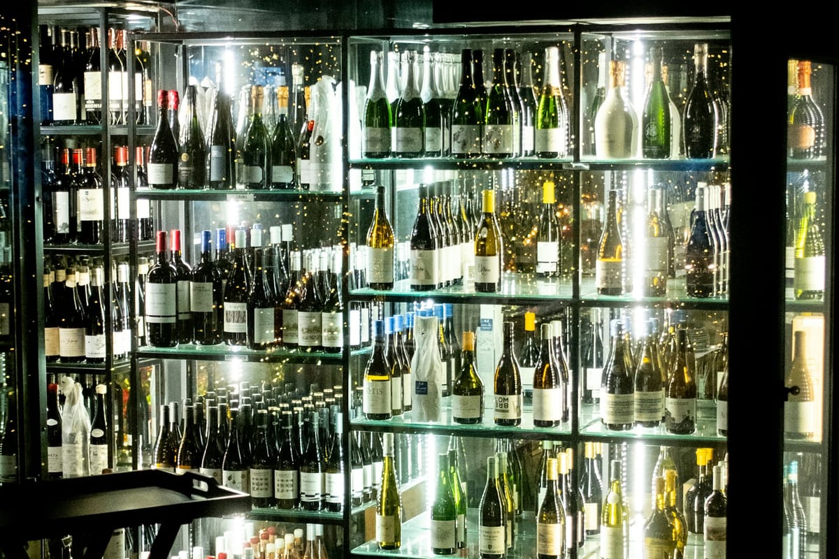 The narrow zinc bar of Maison Velours lit by warm candlelight, rows of wine bottles on dark wooden shelving behind