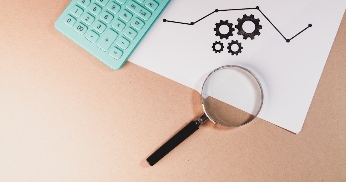 Calculator, magnifying glass, and chart with gears on paper.